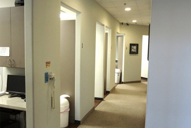 Modern dental office hallway with closed treatment rooms and overhead lighting.